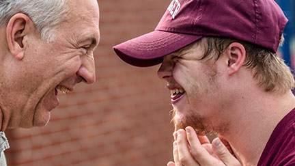 downs syndrome man wearing cap laughing with older gentleman